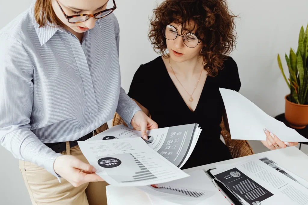 Dos profesionales comparan documentos y gráficos sobre una mesa de trabajo.