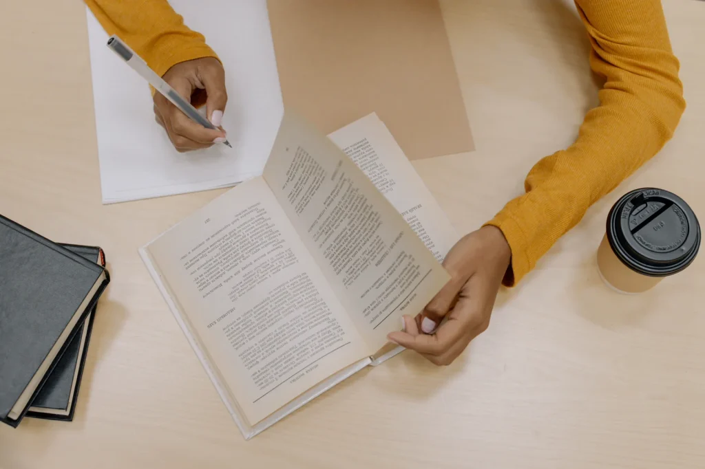 Persona toma notas junto a un libro abierto para recordar y relacionar ideas.