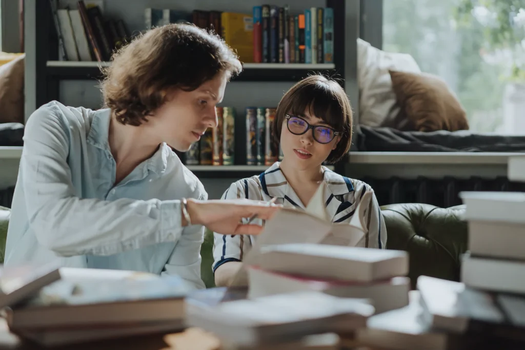 Dos lectores conversan con libros abiertos en una biblioteca.