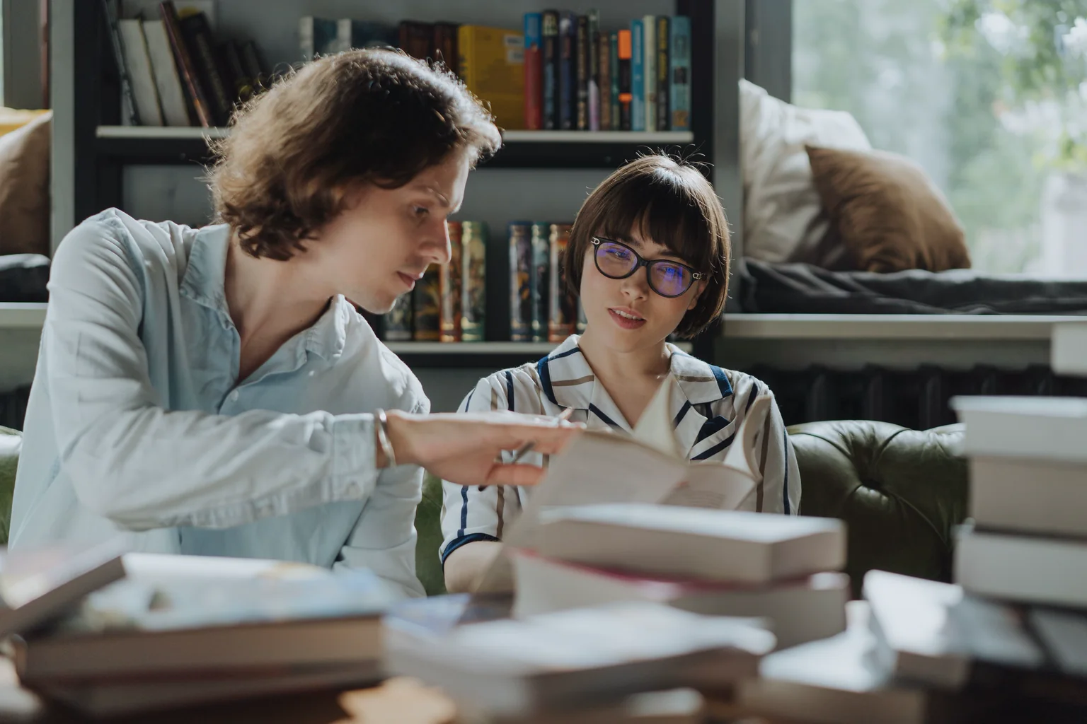 Dos lectores conversan con libros abiertos en una biblioteca.
