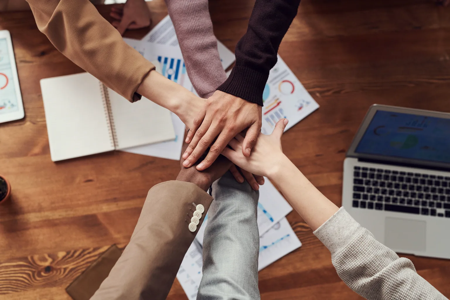 Equipo une sus manos sobre una mesa con gráficos de trabajo al fondo