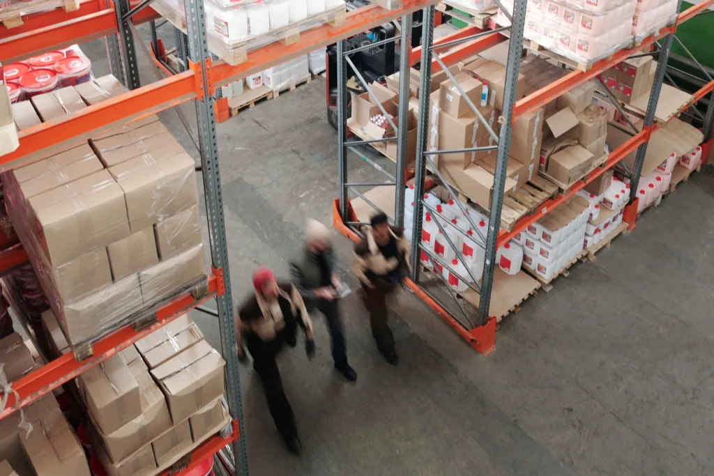 Dos trabajadores recorren un almacén entre estanterías con cajas y productos