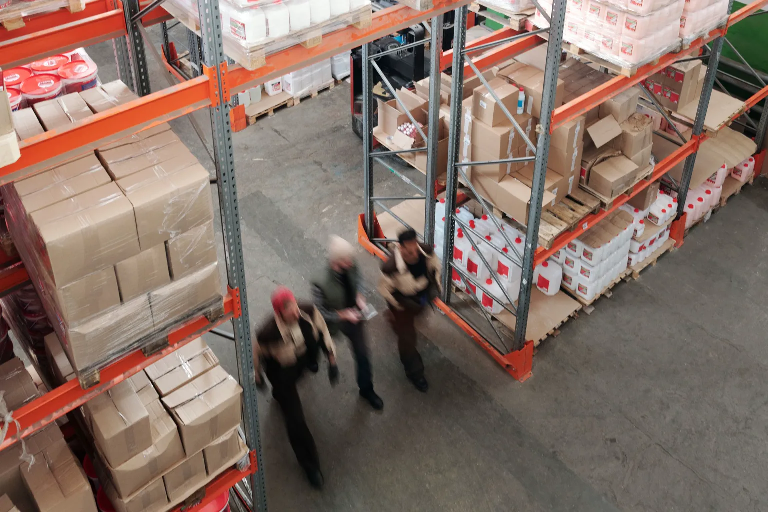 Dos trabajadores recorren un almacén entre estanterías con cajas y productos