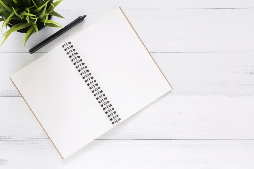 Cuaderno abierto, bolígrafo y planta sobre una mesa como apoyos externos para organizar el pensamiento