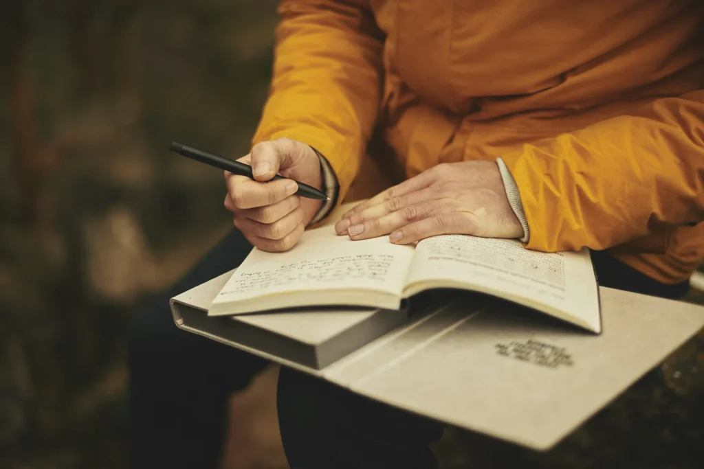 Persona escribe notas a mano sobre un libro abierto mientras estudia.