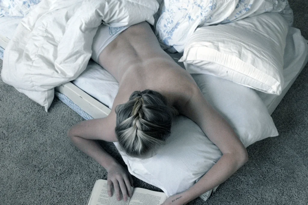 Persona lee un libro recostada entre almohadas antes de dormir.