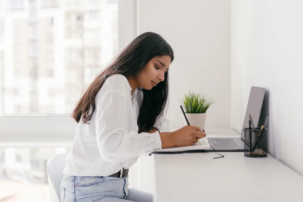 Profesional escribe reflexiones en un cuaderno junto a su computadora portátil